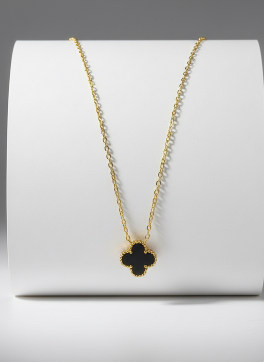 Gold necklace with a clover pendant on a white stand against a gray background