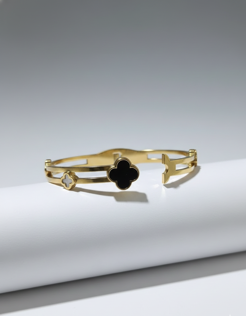 Gold bracelet with a black clover design on a white surface