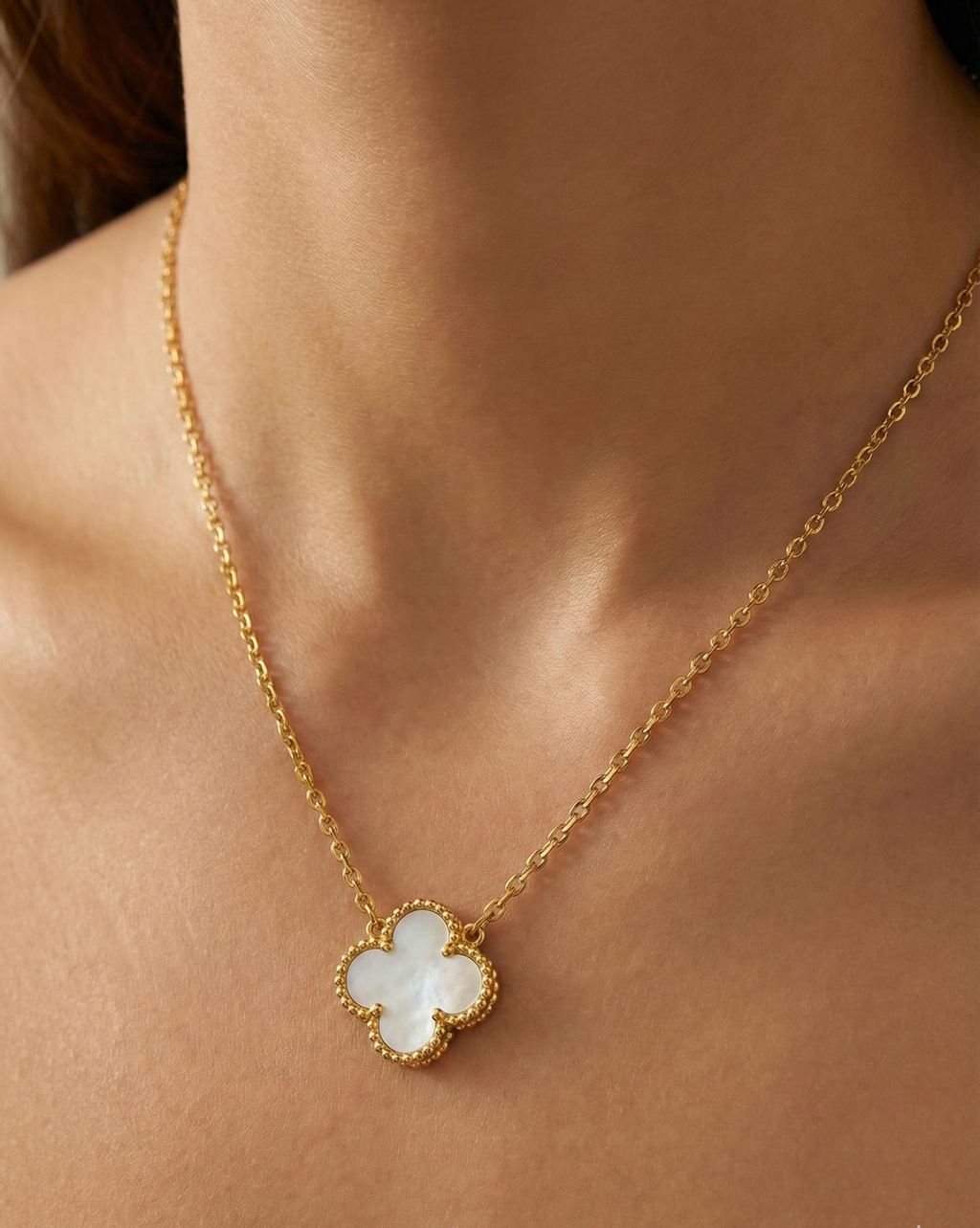 Gold necklace with a clover-shaped pendant on a person's neck