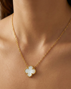 Gold necklace with a clover-shaped pendant on a person's neck