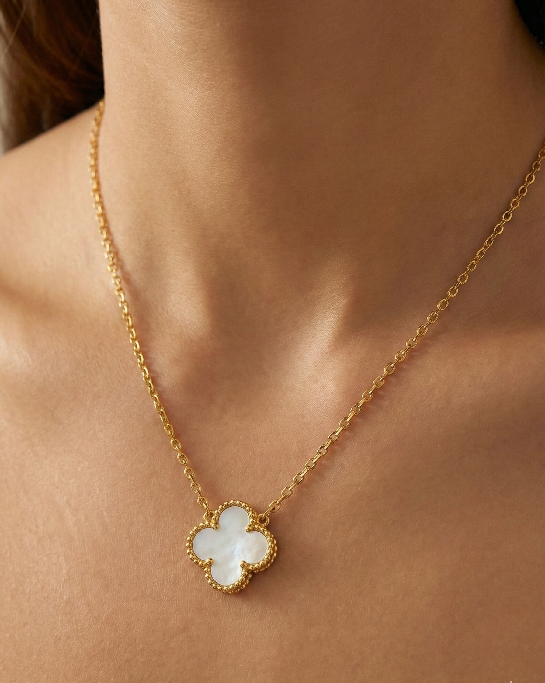 Gold necklace with a clover-shaped pendant on a person's neck