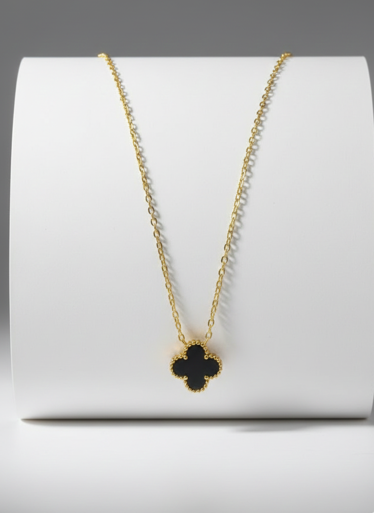 Gold necklace with a clover pendant on a white stand against a gray background