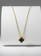 Gold necklace with a clover pendant on a white stand against a gray background