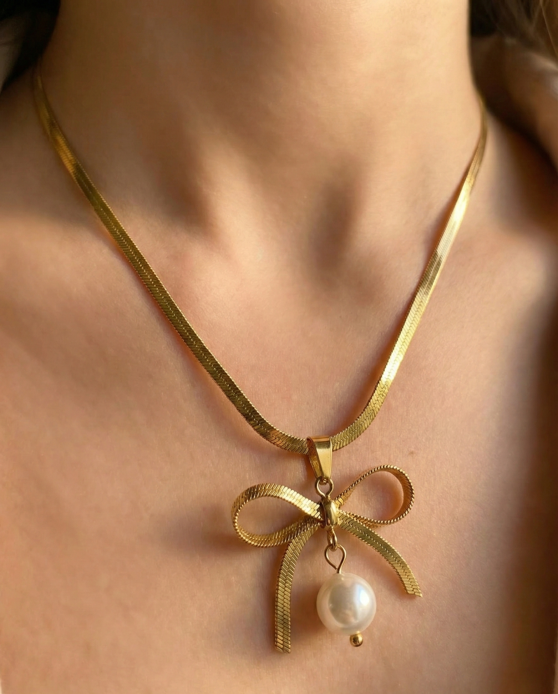 Gold necklace with a bow and pearl pendant on a person's neck