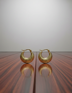 Gold hoop earrings on a reflective surface with a neutral background