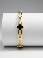 Gold bracelet with black clover design on a white cylindrical stand