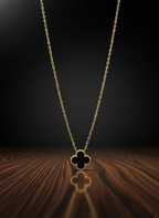 Gold necklace with a clover-shaped pendant on a wooden surface with a dark background